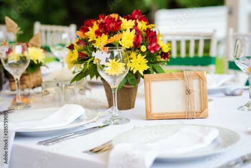 Garden wedding table set up decoration - fresh red and yellow flowers and a blank photo frame/board