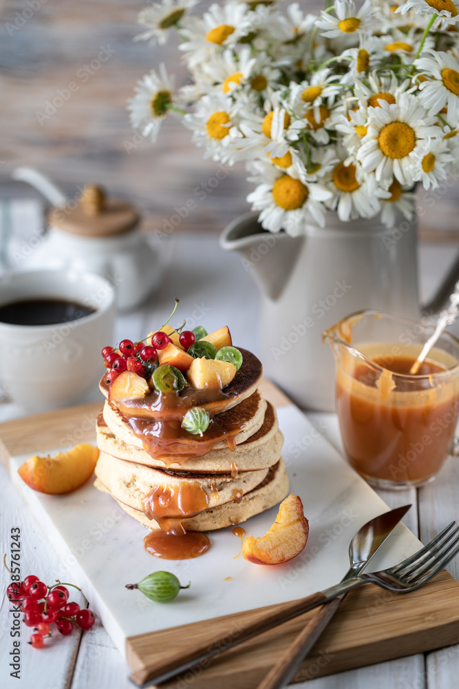 Cornmeal pancakes with salted caramel served with berries and fruits on a white wooden background. Cornmeal pancakes with salted caramel served with berries and fruits on a white wooden background.