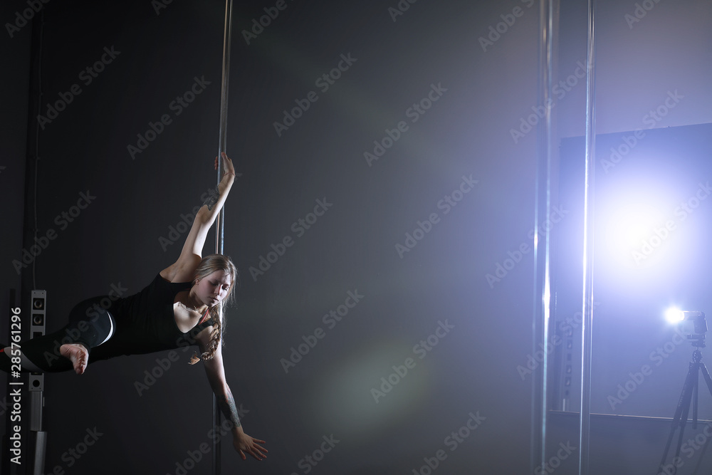 The dancer on the pylon in the studio. Girl doing exercises on a sports equipment. The dancer on the pylon in the studio. Girl doing exercises on a sports equipment.