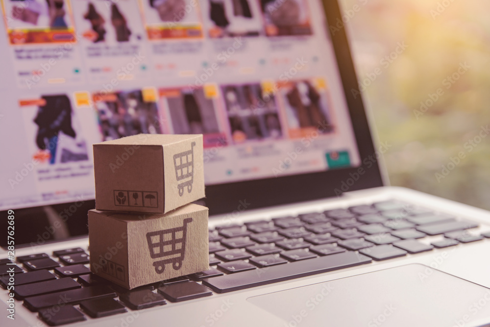 Online shopping - Paper cartons or parcel with a shopping cart logo on a laptop keyboard. Shopping service on The online web and offers home delivery. Online shopping - Paper cartons or parcel with a shopping cart logo on a laptop keyboard. Shopping service on The online web and offers home delivery.