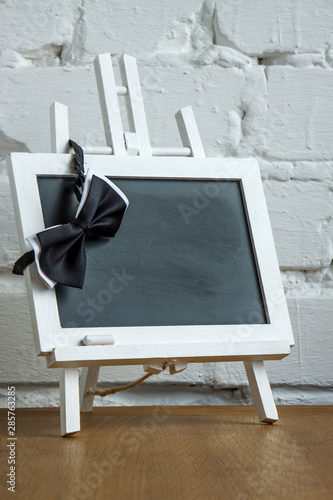 Close-up of a miniature chalk board and bow tie on a white brick wall background, selective focus
