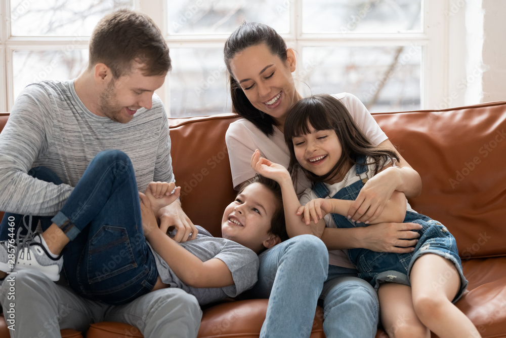 Happy parents with children tickling laughing playing on sofa together Happy parents with children tickling laughing playing on sofa together