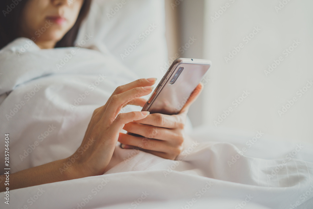 Asian Girl in bed room on the bed with the mobile phone.Closeup portrait of young sleepy exhausted woman lying in bed using smartphone, Asian Girl in bed room on the bed with the mobile phone.Closeup portrait of young sleepy exhausted woman lying in bed using smartphone,