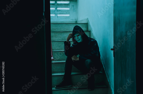Portrait of white mask and hoodie sitting on old stairs. Selective focus on hands. Sadness, despair, dark, concept