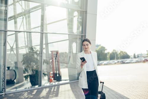 Businesswoman on commute transit talking on the smartphone while walking with hand luggage in train station or airpot going to boarding gate. Asian woman happy using mobile phone app for conversation.