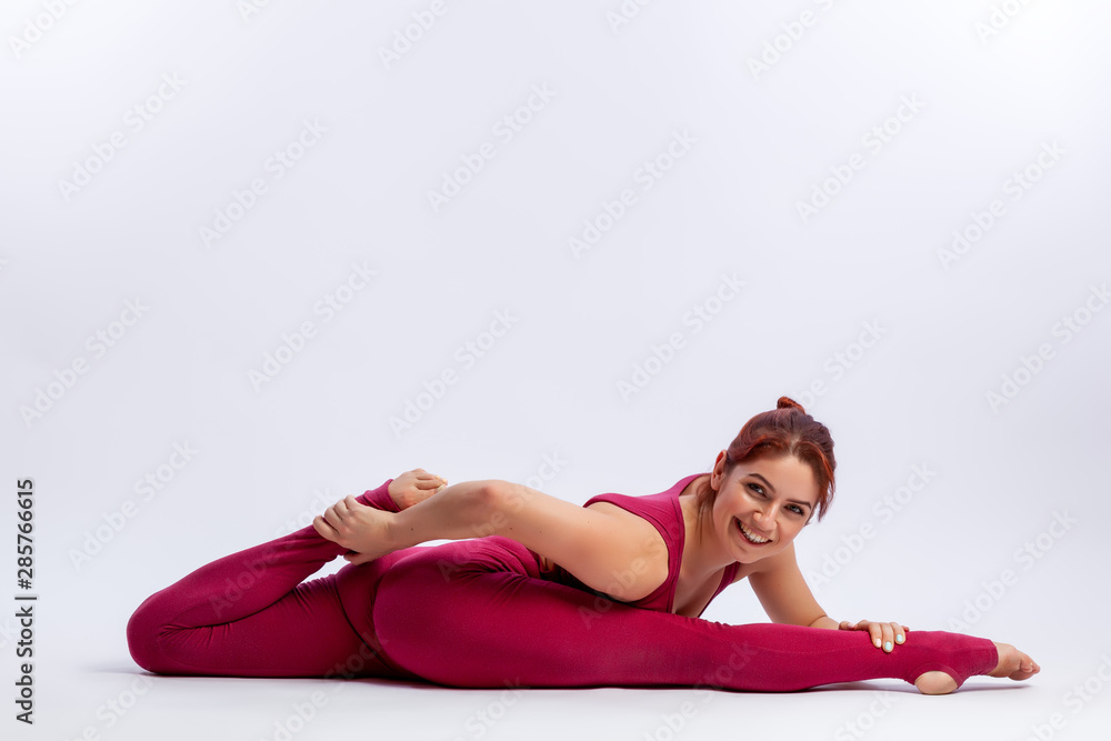 Young athletic woman gymnast in gymnastic jumpsuit does stretching in difficult poses on a white-lined background. The concept of female beauty, sport and grace. Young athletic woman gymnast in gymnastic jumpsuit does stretching in difficult poses on a white-lined background. The concept of female beauty, sport and grace.