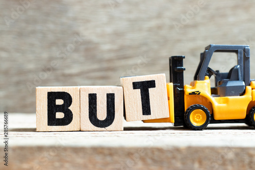 Toy forklift hold letter block t to complete word but on wood background
