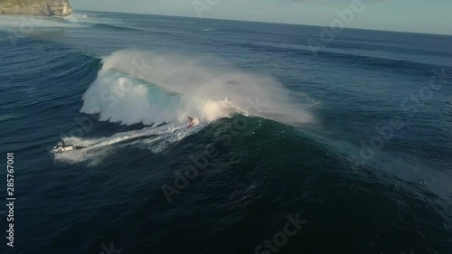 Man on a jet ski helps his surfer friend pick up speed from a big wave