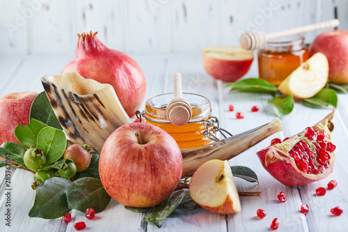 Rosh hashanah - jewish New Year holiday concept. Traditional symbols: Honey jar and fresh apples with pomegranate and shofar horn on white wooden background. Copy space for text. photo