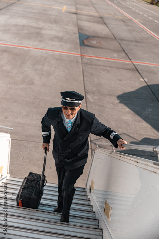 Mature happy pilot with suitcase lifting up the plane ladder Mature happy pilot with suitcase lifting up the plane ladder