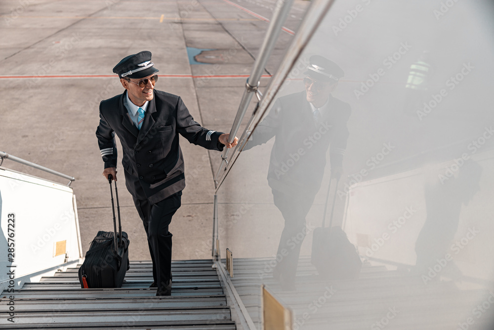 Adult happy pilot with suitcase going up the plane ladder Adult happy pilot with suitcase going up the plane ladder