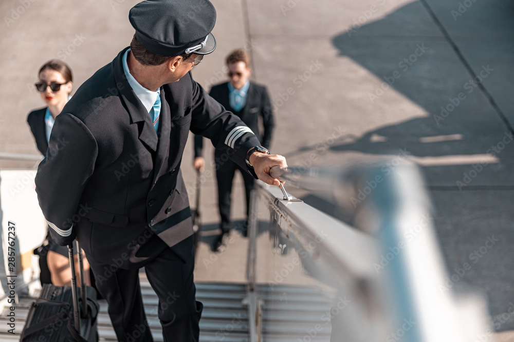 Fototapeta premium Caucasian pilot with suitcase going up the plane ladder