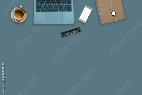 Laptop on green desktop in modern office with accessories - top view on desk from above.