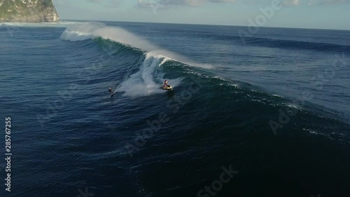 Man on a jet ski helps his surfer friend pick up speed from a big wave
