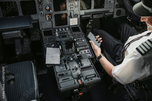 Adult pilot in cockpit looking at screen of his smartphone