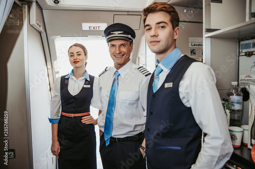 Leinwand Poster Smiling Caucasian pilot with flight attendants standing on airplane board
