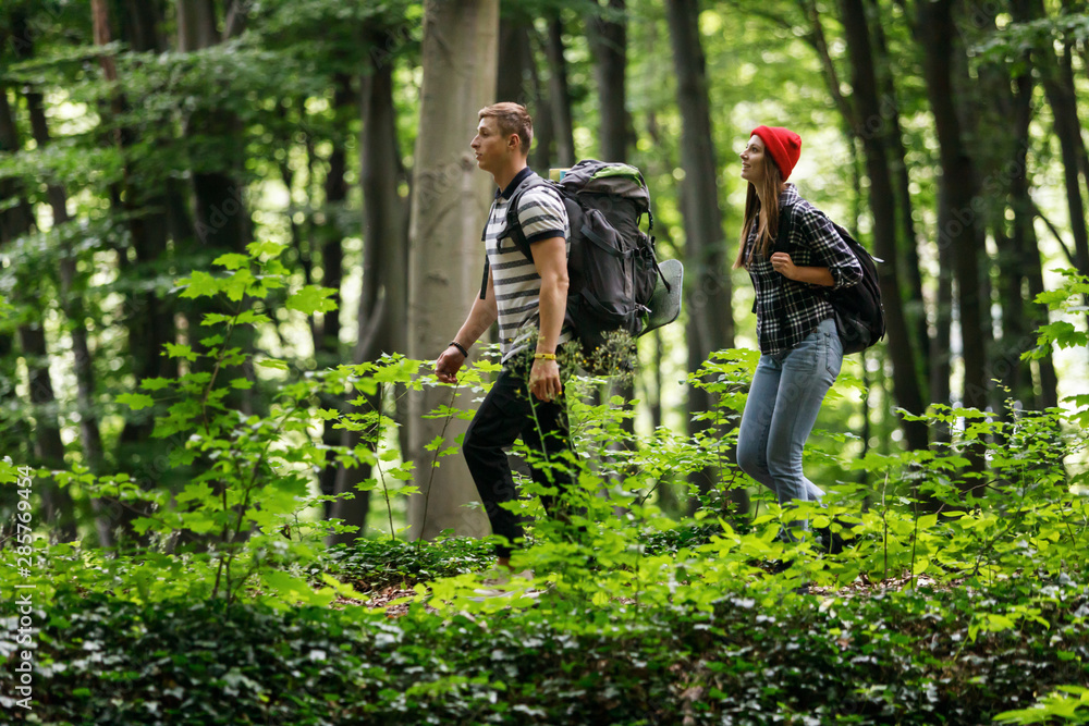Happy young couple standing together with backpacks while hiking in the forest