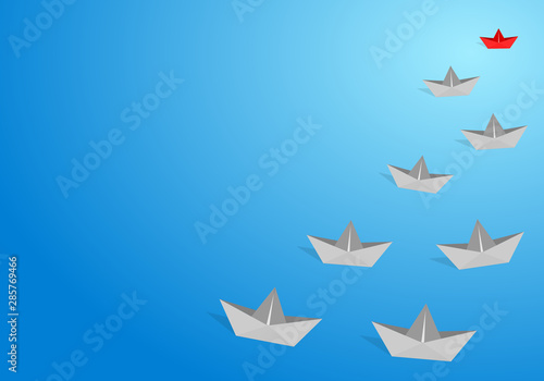 Red origami paper boat leading gray staff ones go on the route on blue background. Leadership and teamwork concept.