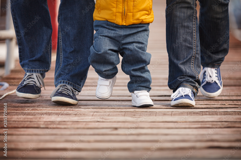 Closeup of a family dressed in casual clothes walking along wooden flooring. Mom, dad and child step on a wooden pier on a cool autumn or spring day. Closeup of a family dressed in casual clothes walking along wooden flooring. Mom, dad and child step on a wooden pier on a cool autumn or spring day.