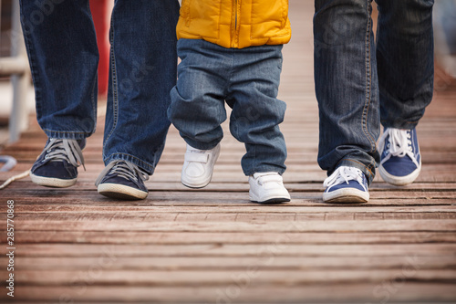 Closeup of a family dressed in casual clothes walking along wooden flooring. Mom, dad and child step on a wooden pier on a cool autumn or spring day.