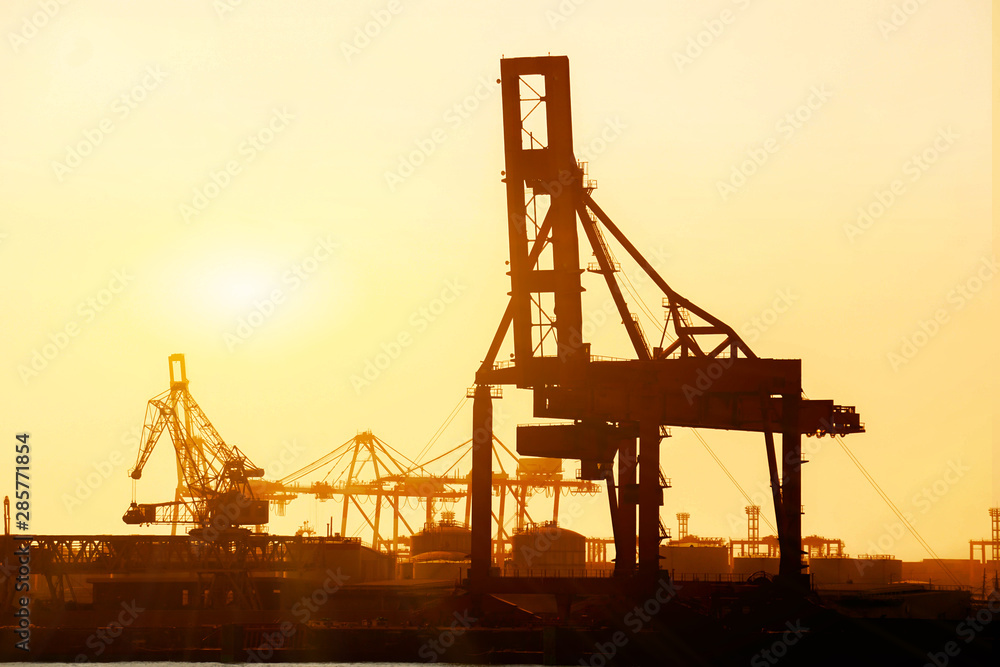 Closeup and silhouette of container and gantry crane at Osaka port are loading on evening and sun flares  background.