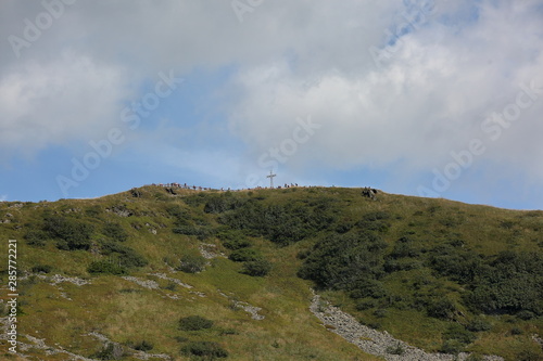 Landscapew with Tarnica peak in Bieszczady mountains, crowd of tourists nearby steel cross at top, clouds over it