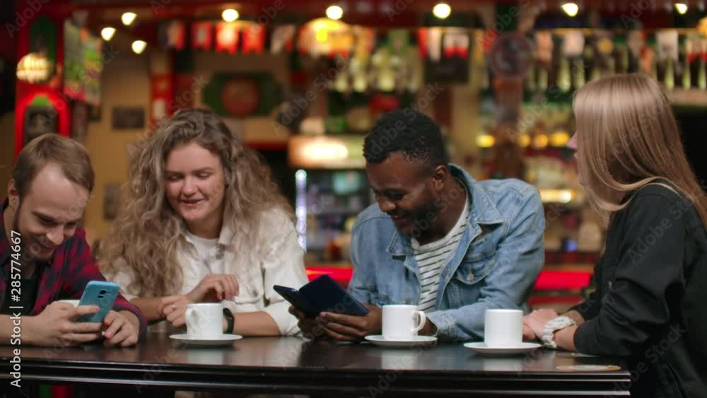 A cheerful company of friends in a restaurant discuss photos on smartphones and laugh A cheerful company of friends in a restaurant discuss photos on smartphones and laugh