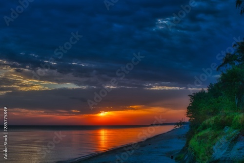 wschód słońca nad Bałtykiem w okolicach Dziwnowa, chmury i słońce odbijają się w spokojnej wodzie morza