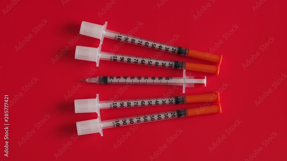 A set of insulin syringes with caps and without caps on a table with a red surface. Close up