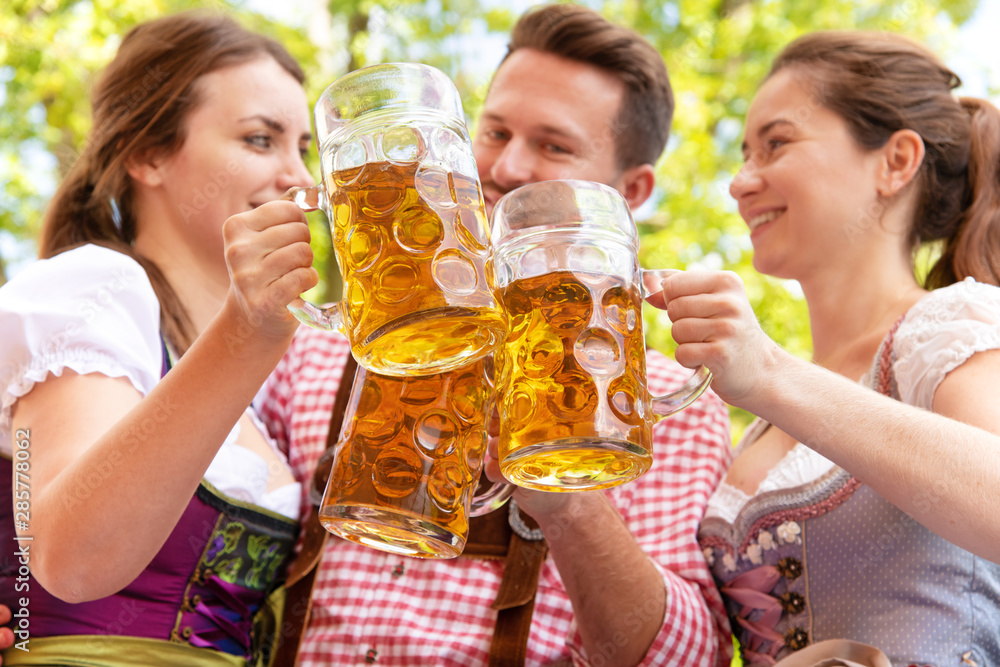 Young people in Tracht, Dindl and Lederhosen having fun in Beer garden Young people in Tracht, Dindl and Lederhosen having fun in Beer garden