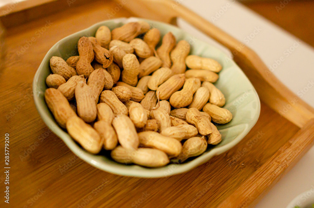 DRIED PEANUTS IN A GREEN BOWL ON A WOODEN TRAY DRIED PEANUTS IN A GREEN BOWL ON A WOODEN TRAY