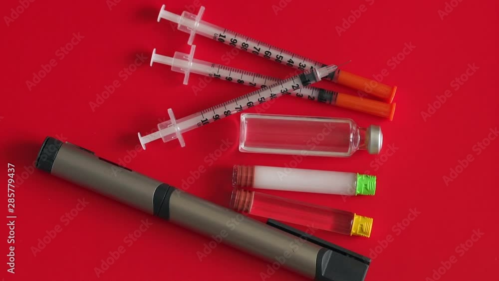 Insulin syringes, insulin pen, insulin ampoules on a table with a red