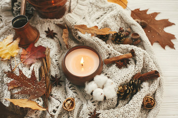 Hygge lifestyle. Candle with berries, fall leaves, anise,herbs, acorns, nuts , cinnamon, cotton on white knitted sweater. Autumn mood. Hello autumn, cozy inspirational image