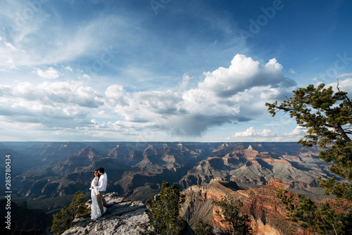 A couple stands far on the edge of a cliff with a spectacular view of the canyon, a stunning sky with clouds