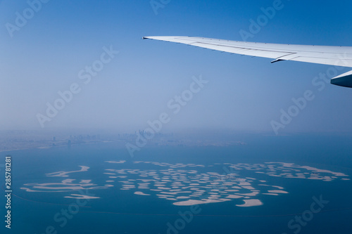 Airplane Wing and Clouds Viewed from Inside the Aircraft, with Dubai The World Islands in background. Travel concept with copy space.