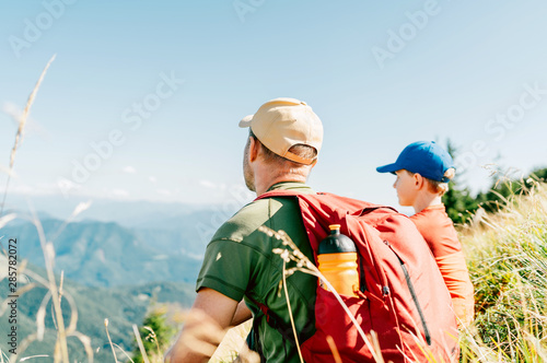 Father and his teenage son sitting on the grass and enjoying mountain landscape during their weekend hiking walking.