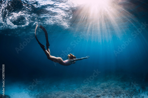Woman freediver glides with fins. over sandy sea. Freediving and beautiful light in blue sea photo