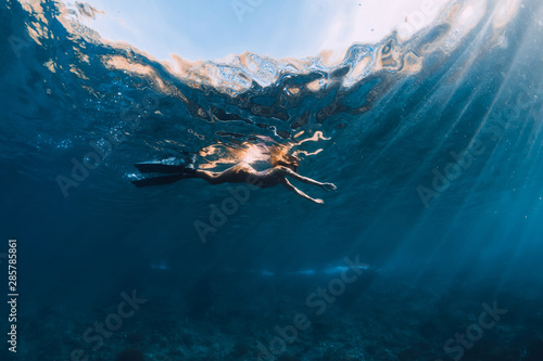 Woman swimming with fins in blue ocean. Underwater view