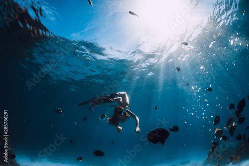 Freediver girl with fins dive with fishes in blue sea