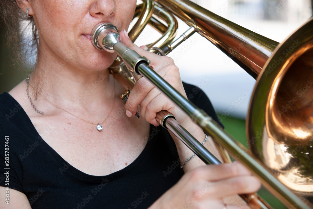 Obraz premium Girl learning to play trombone. Portrait of a girl on a background of a city park park.