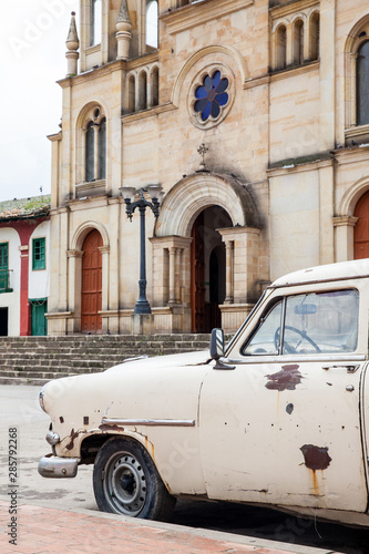 Antique rusty car parked next to the Parish Church of the small town of Ventaquemada in Colombia