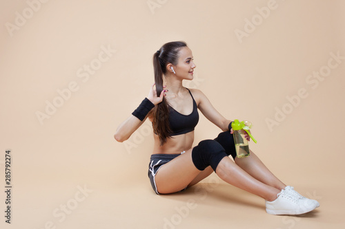 Young athletic girl brunette with black knee-pads sits on the floor, rests after a workout, takes a break.