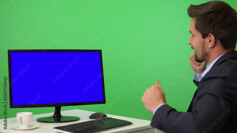 A young businessman sits in front of a computer with blue screen and dances - green screen studio A young businessman sits in front of a computer with blue screen and dances - green screen studio