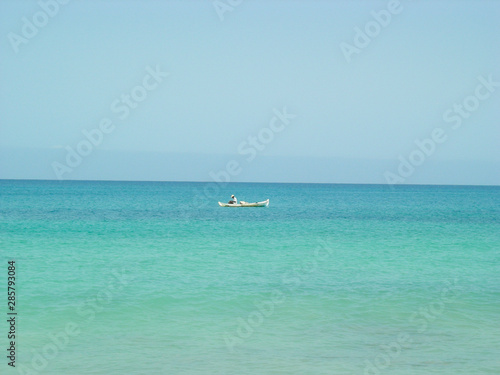 Sea and blue sky, horizon line and man in a white canoe