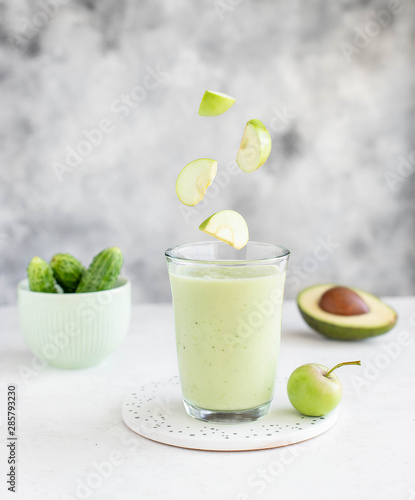 glass of smoothie with avocado cucumber and flying apple slices on a light background. healthy food concept