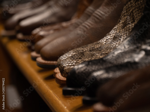 A pair of snake skin boots on a wooden shelf full of cowboy boots in a store for country and western apparel with a shallow depth of field focused only on the reptile skinned footwear standing out.