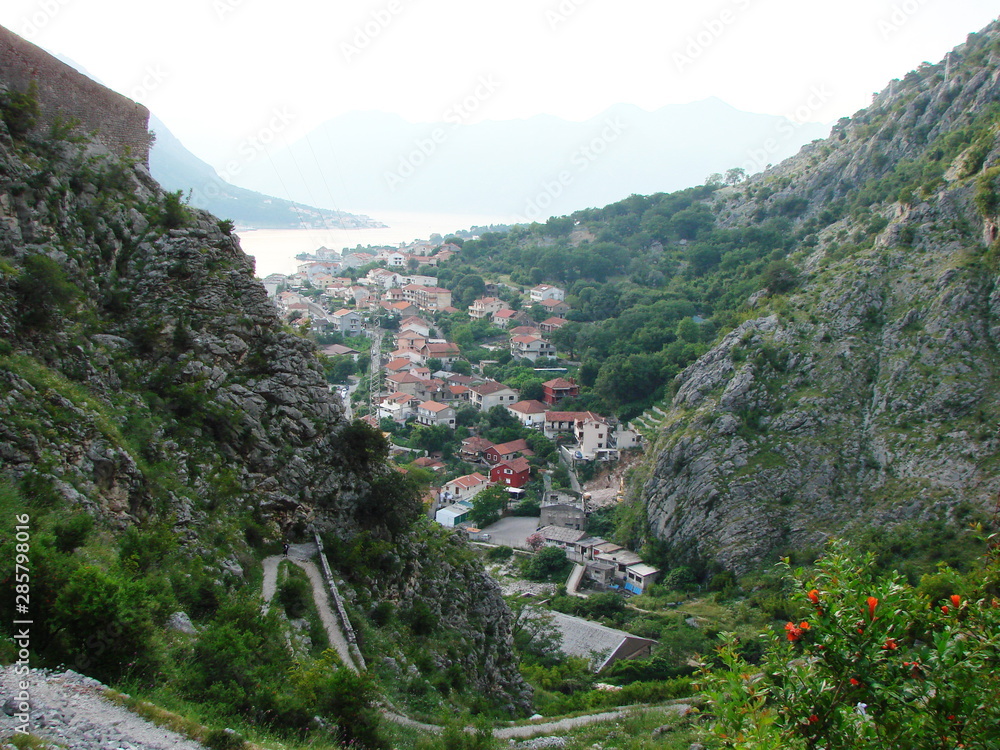 The view from the top of the mountain to the evening town is squeezed on both sides by high steep cliffs against the backdrop of the gulf of the sea on the horizon.