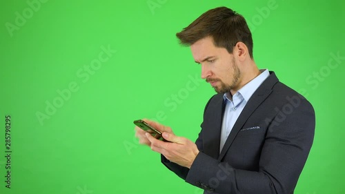 A young handsome businessman tries to make a broken smartphone work, gets angry - green screen studio photo