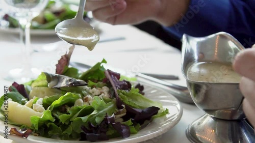 man wearing a blue shirt is pouring ranch salad dressing on his meal at a luxury dinner table during a banquet. the fine dining at the venue serves great delicious dish for people to eat