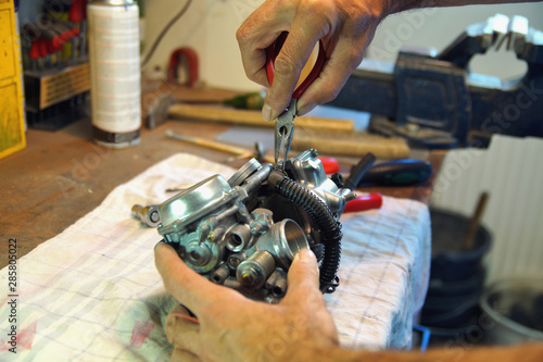 motorcycle carburetor. Automotive Carburetor Repair. Male Using A tong To Rebuild A Carburetor On A Workbench. Mechanic man checking carburetor of motorcycle. Repair. Maintenance and fixing concept.   photo